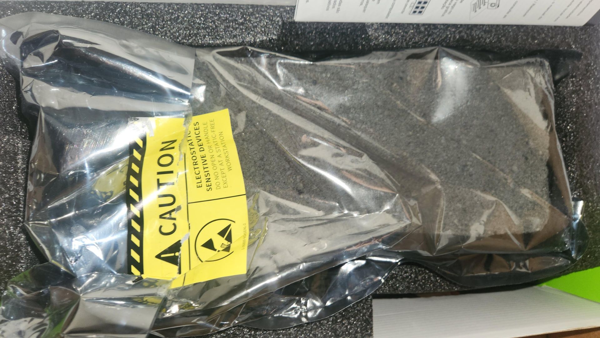 Unbranded electronic device in antistatic packaging with yellow CAUTION label indicating sensitivity.