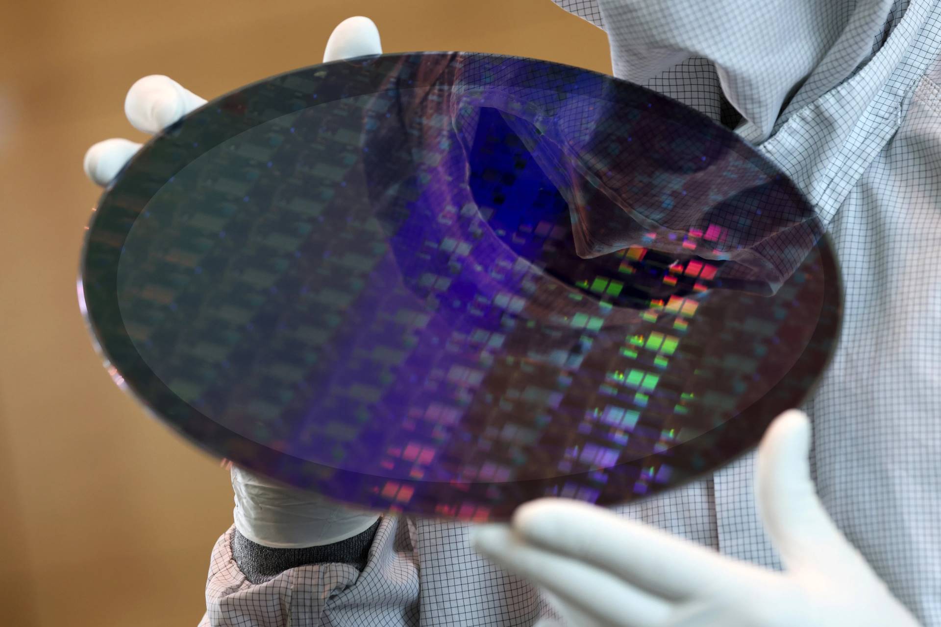 Technician holding a silicon wafer in a cleanroom environment, showcasing microchip technology.