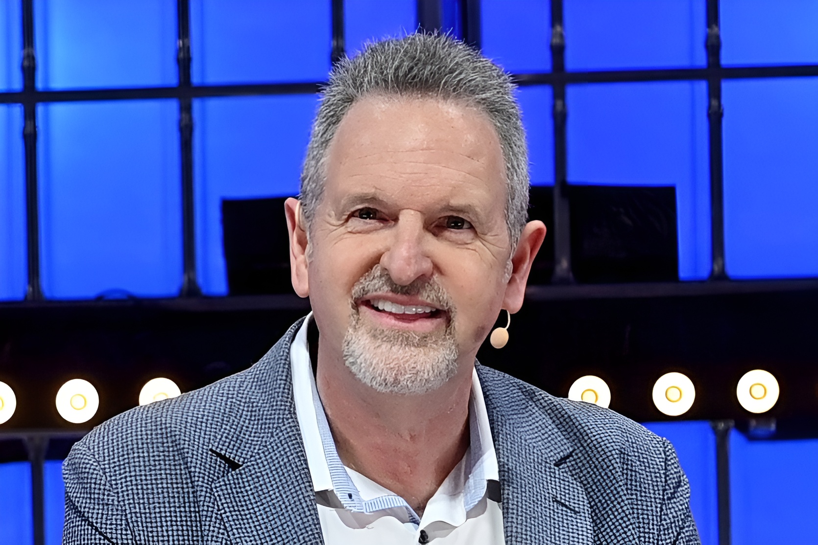 Unbranded person wearing a microphone on stage with blue background.