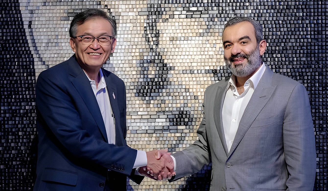 Two men in business suits shaking hands in front of a mosaic wall.
