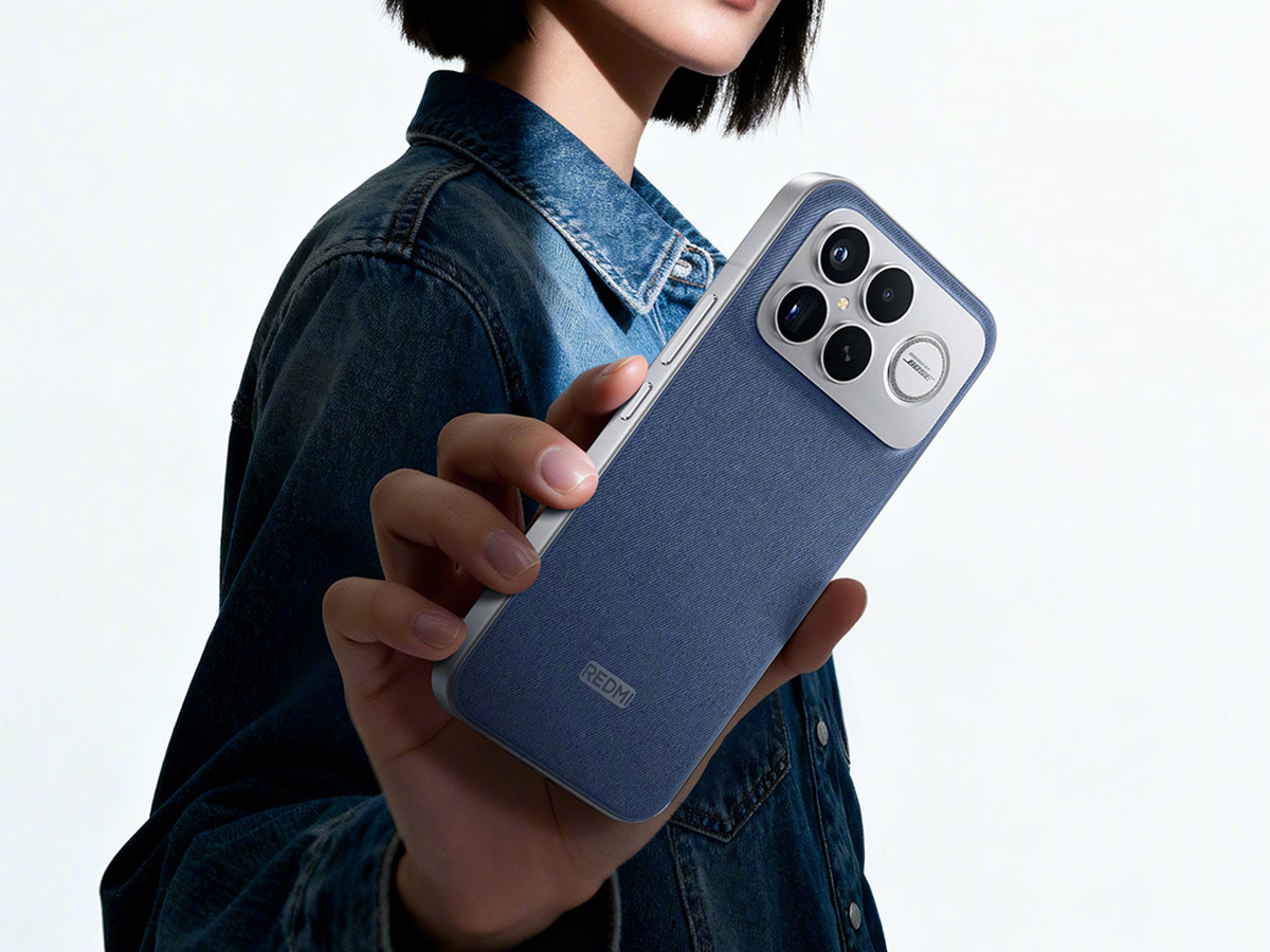 Redmi smartphone with triple camera, held by a person in a denim jacket.