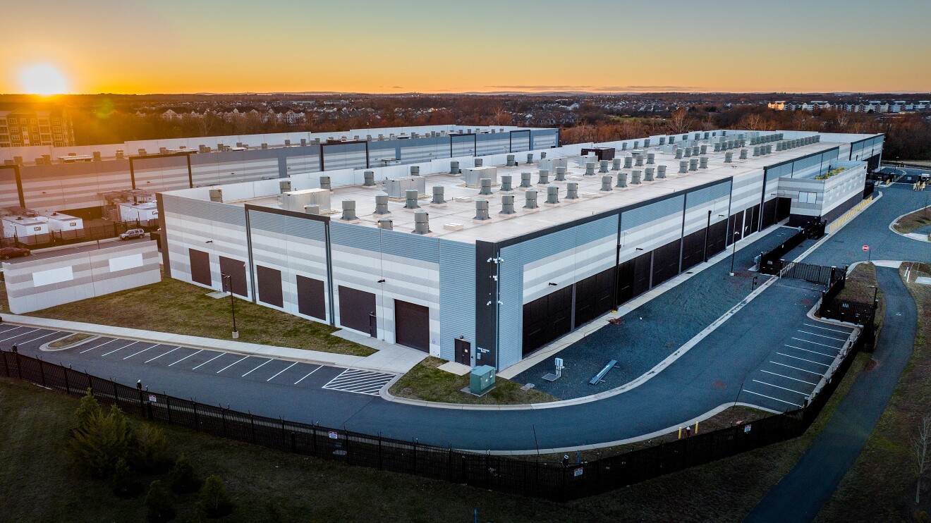 Large unbranded warehouse building at sunset with numerous rooftop HVAC units and an empty parking lot.