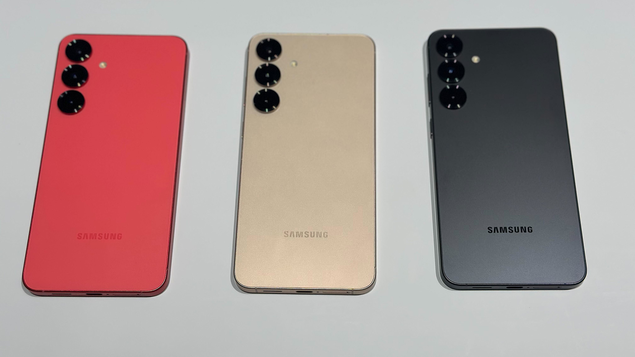Three Samsung smartphones are laid out flat in red, gold, and black colors, each with a triple camera setup.