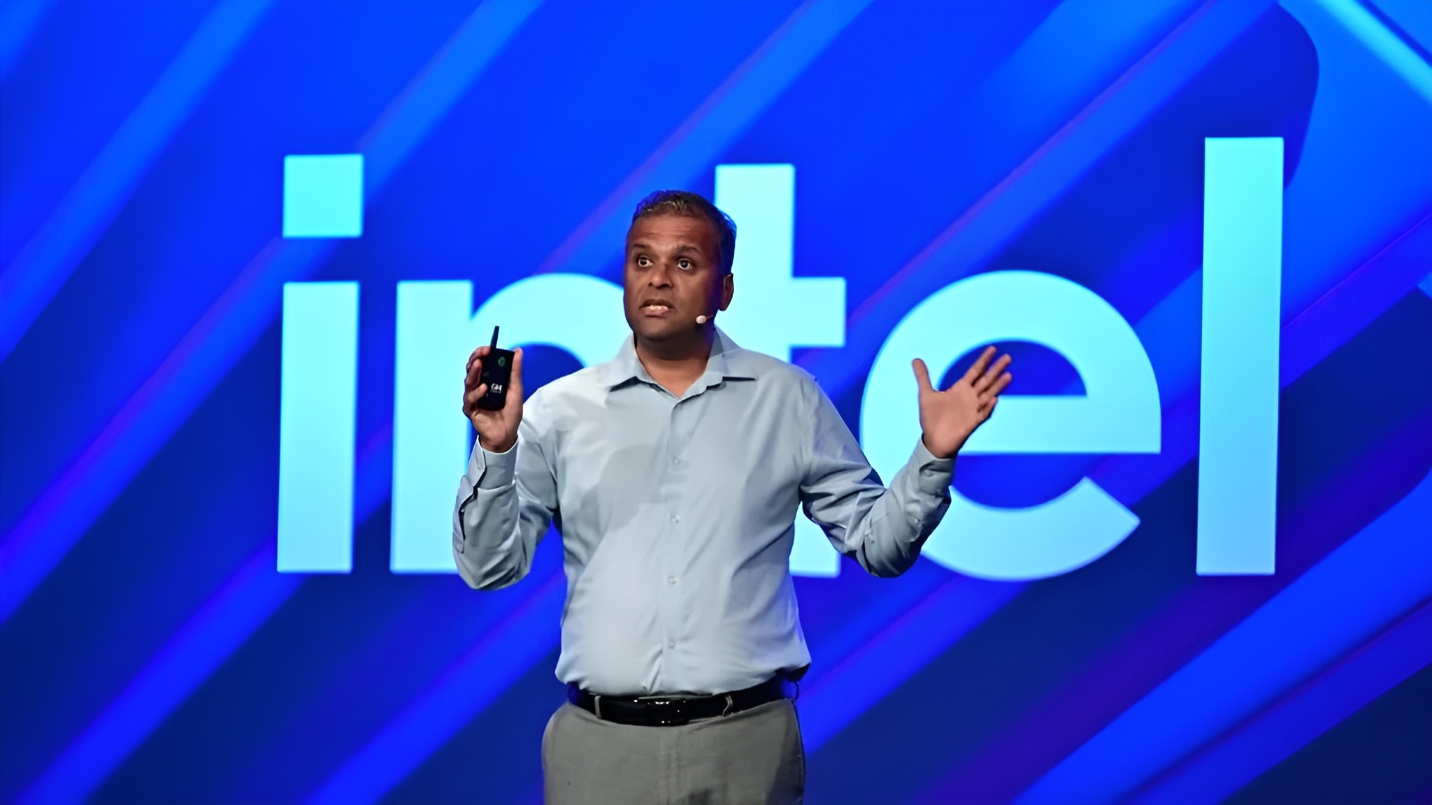A presenter in front of a large intel logo on stage, holding a device in one hand.