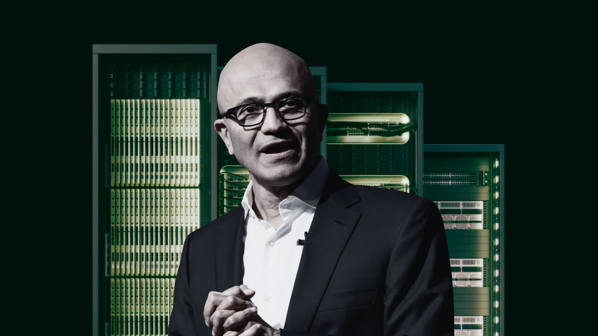 Man in a suit stands in front of a row of server racks.