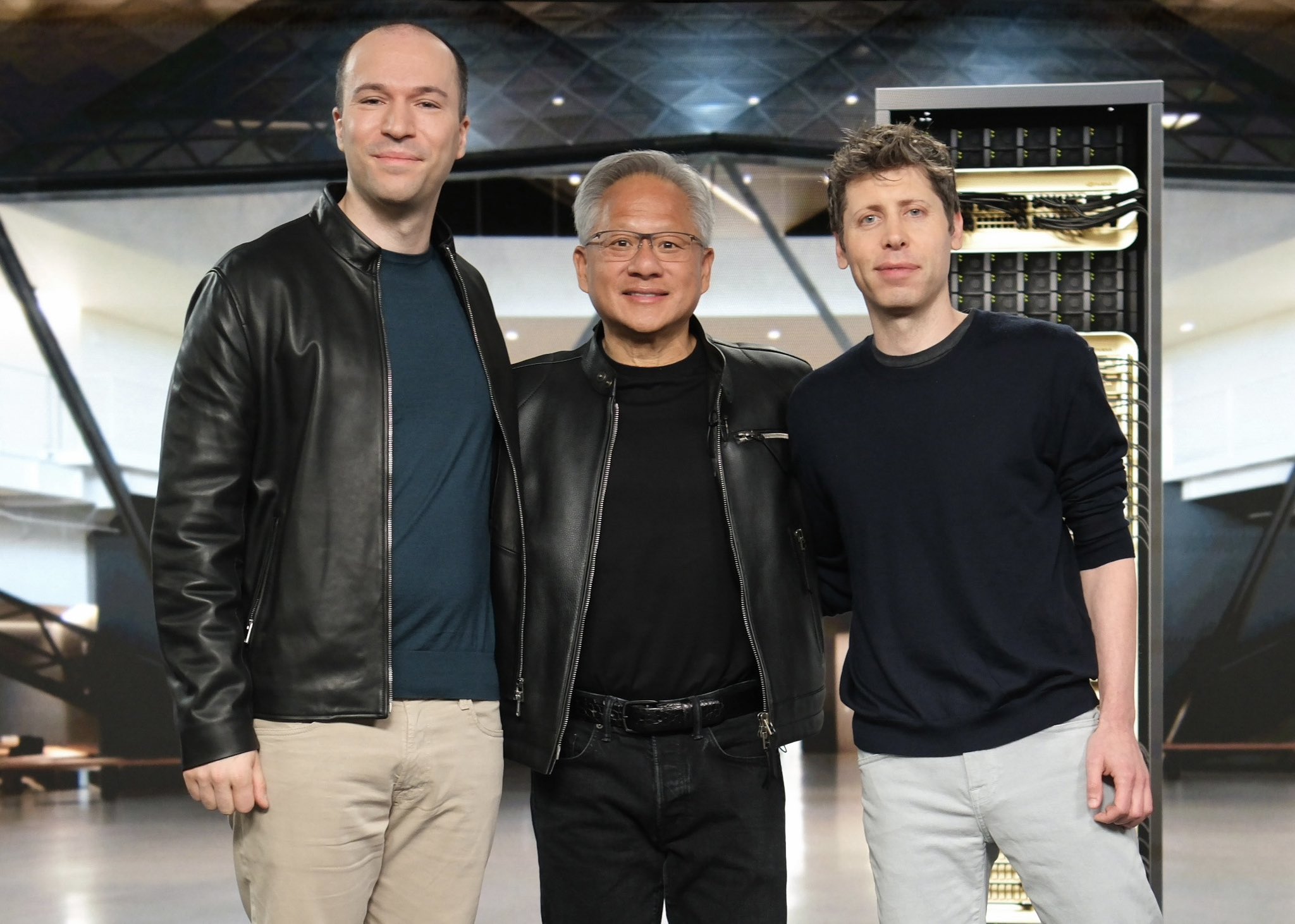 Three individuals standing in front of a large NVIDIA DGX H100 system in a modern interior setting.