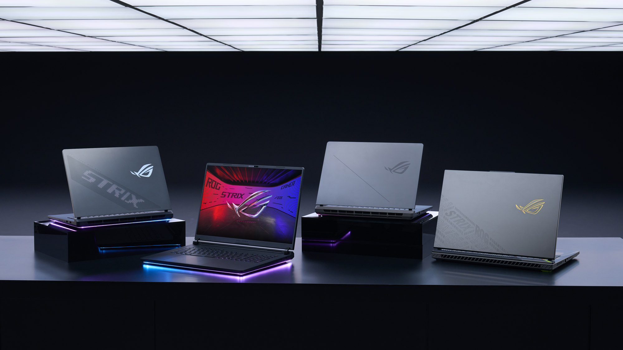 Four ASUS ROG Strix laptops are displayed on a table, with one laptop screen showing 'ROG Strix' on a colorful background.