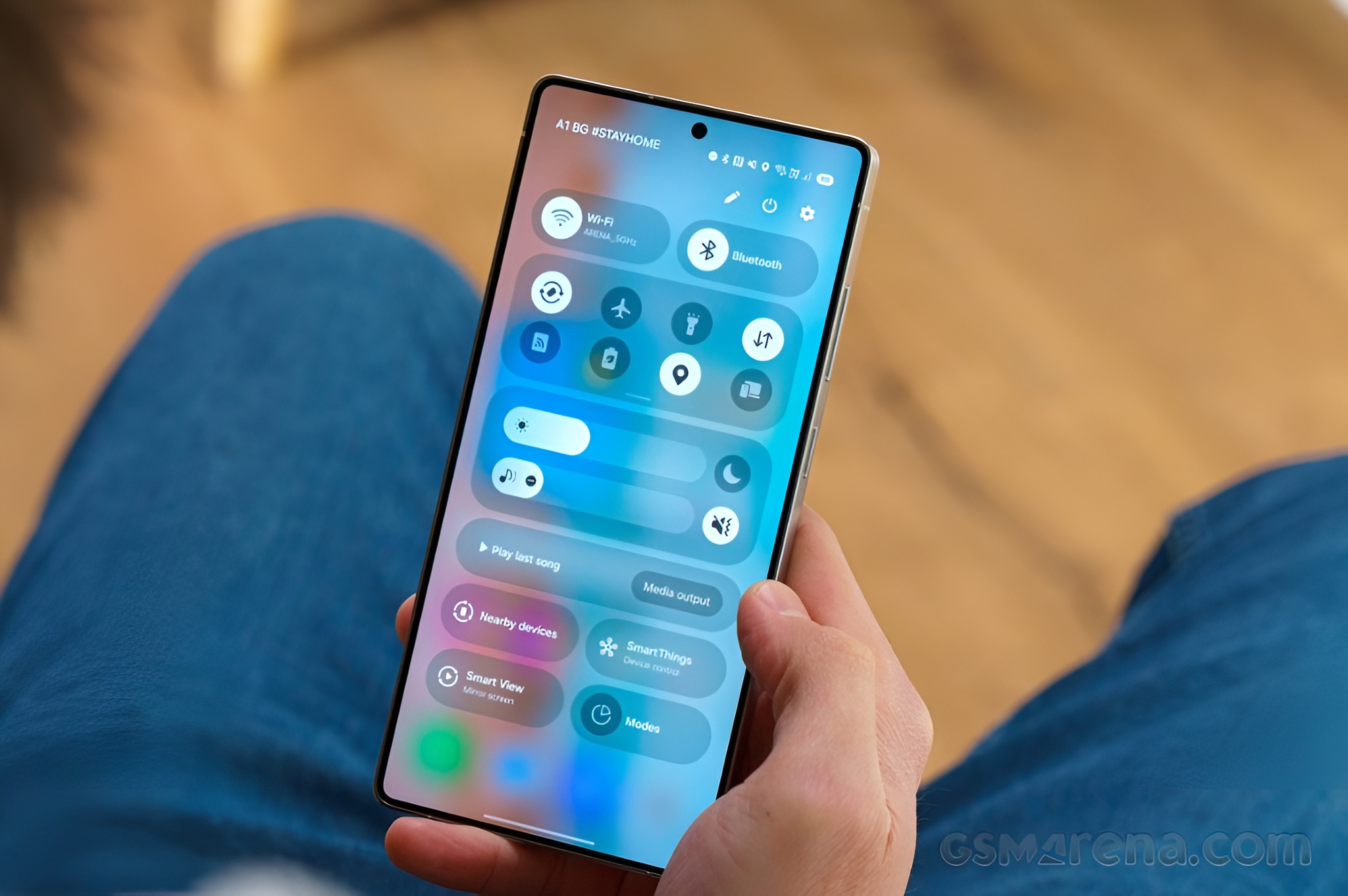 A Samsung Galaxy smartphone displaying the quick settings panel is held in front of a person wearing blue jeans, with 'A1 BG #STAYHOME' visible at the top.