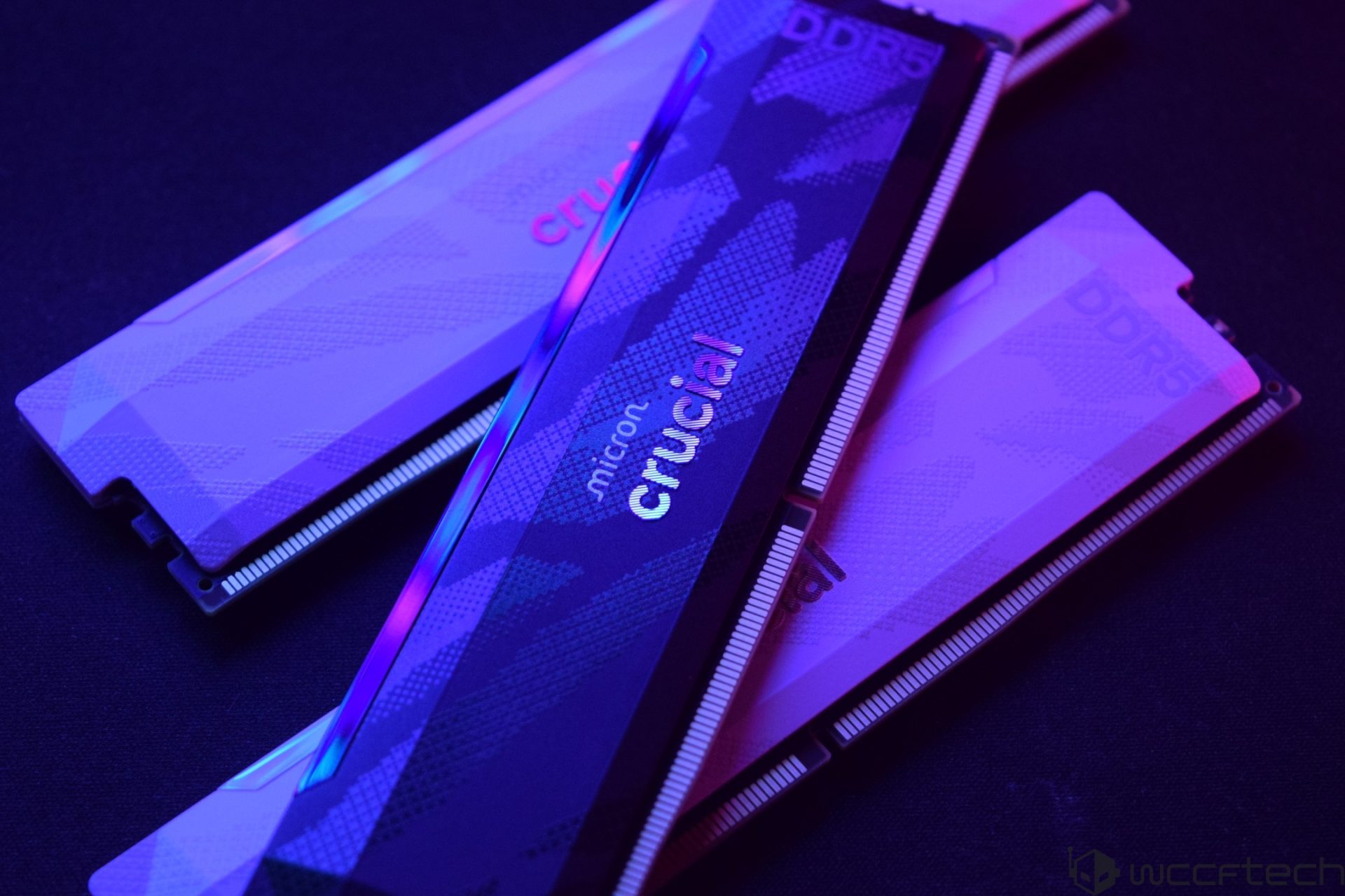 Three Micron Crucial DDR5 RAM modules in a staggered arrangement under blue and pink lighting.