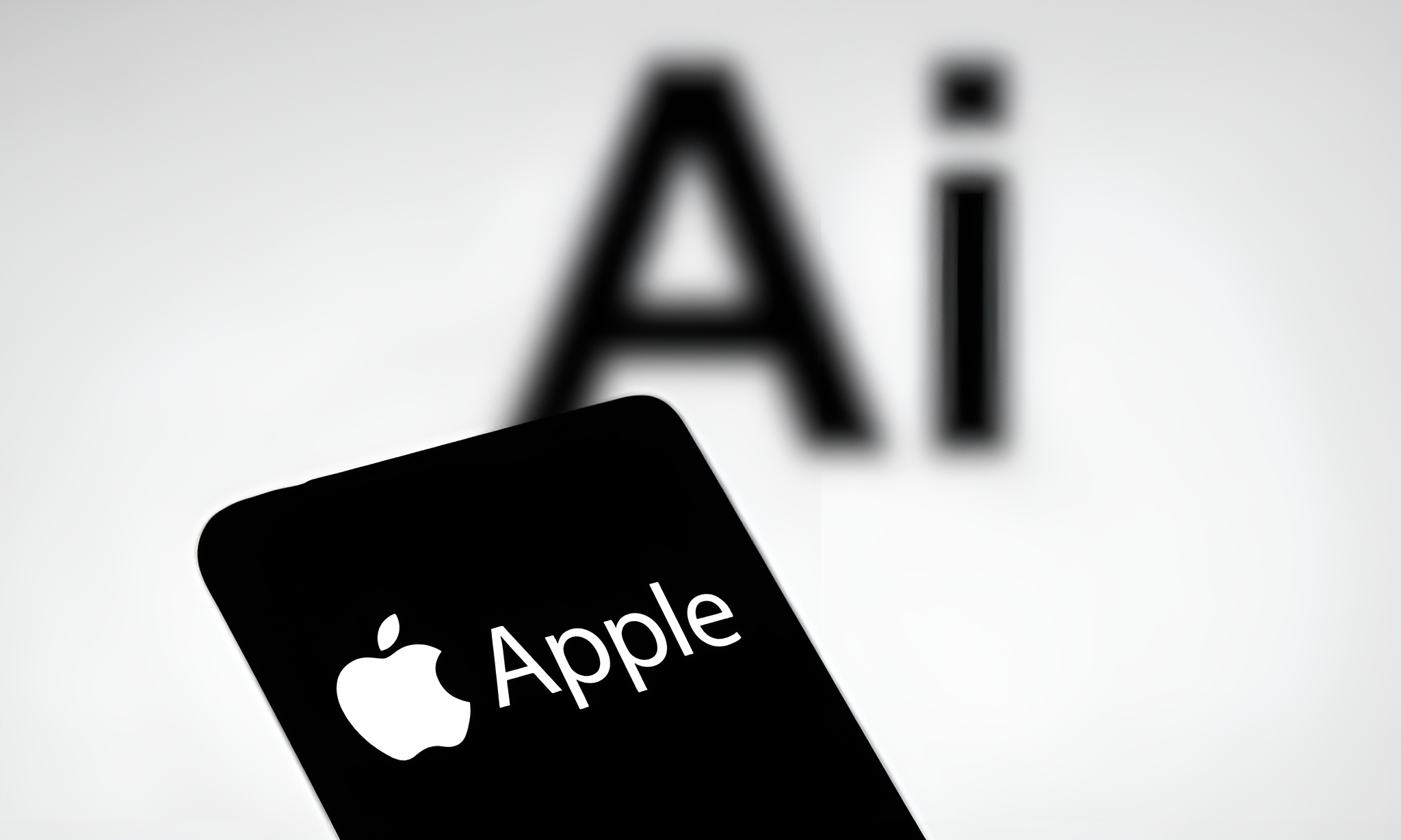 A smartphone screen displaying the Apple logo with the text Apple, in front of a blurred background with large letters