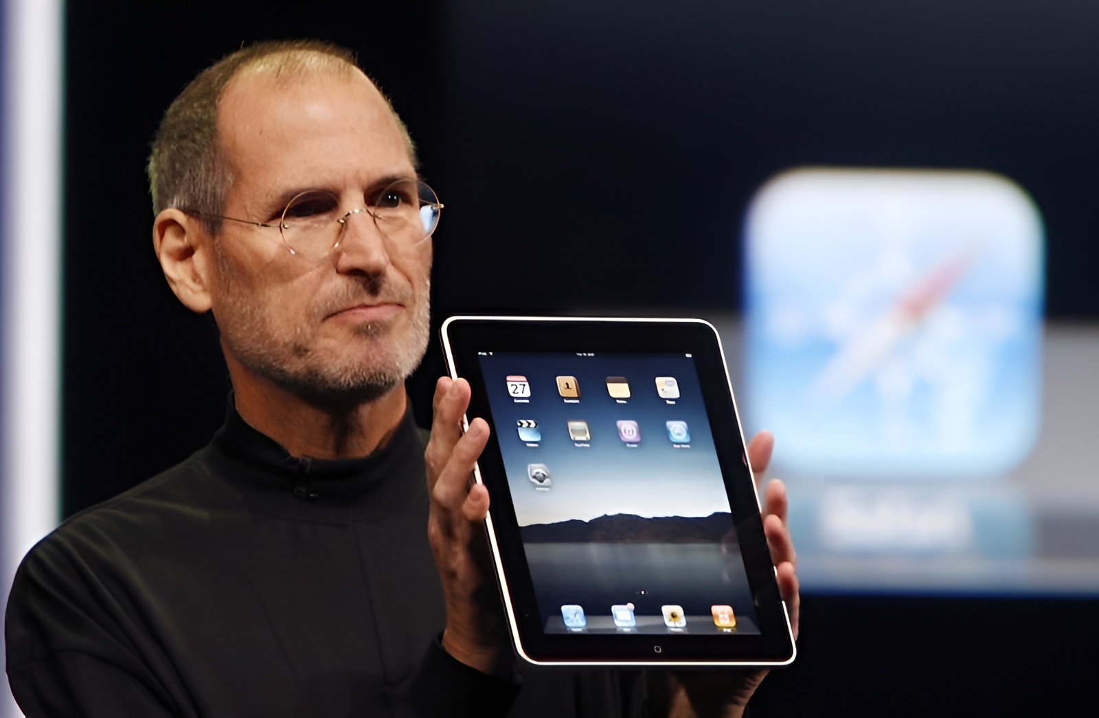 A person holding an Apple iPad with the home screen visible, showing app icons like 'Photos' and 'Safari.'
