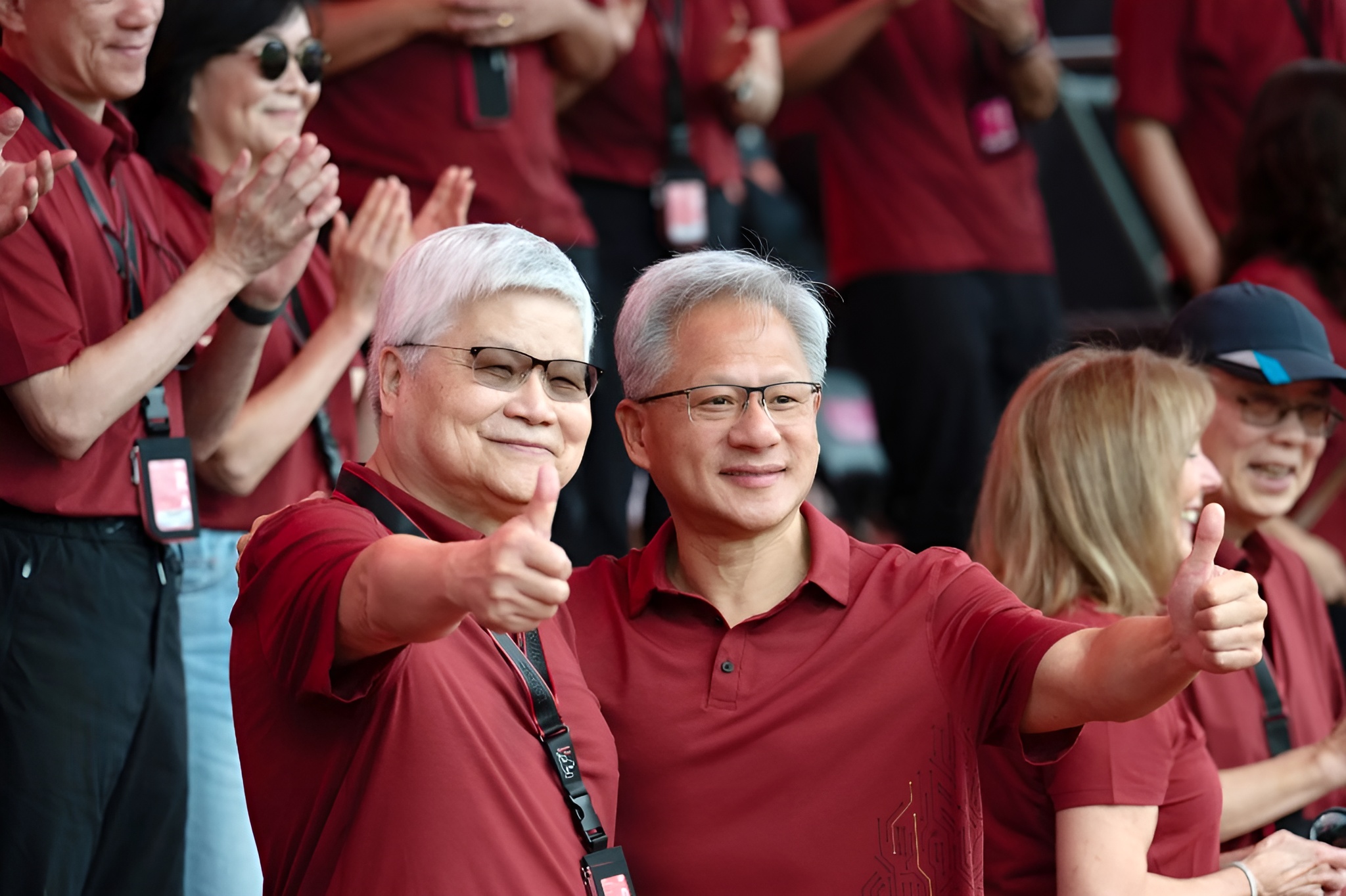Two men in red shirts giving thumbs up while others applaud in the background.