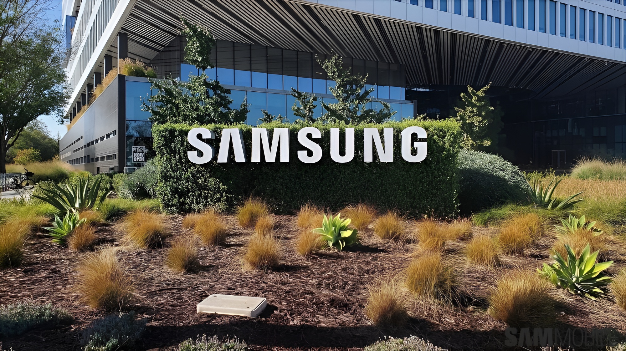A large 'SAMSUNG' sign is prominently displayed in front of a modern Samsung office building surrounded by landscaped