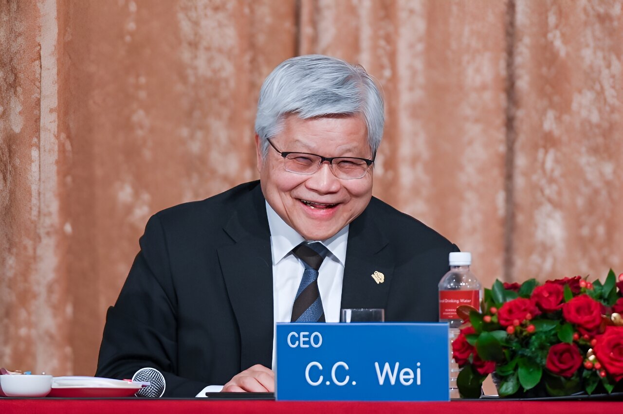 A person with a nameplate reading 'CEO C.C. Wei' seated at a table with a microphone, water bottle, and red roses.