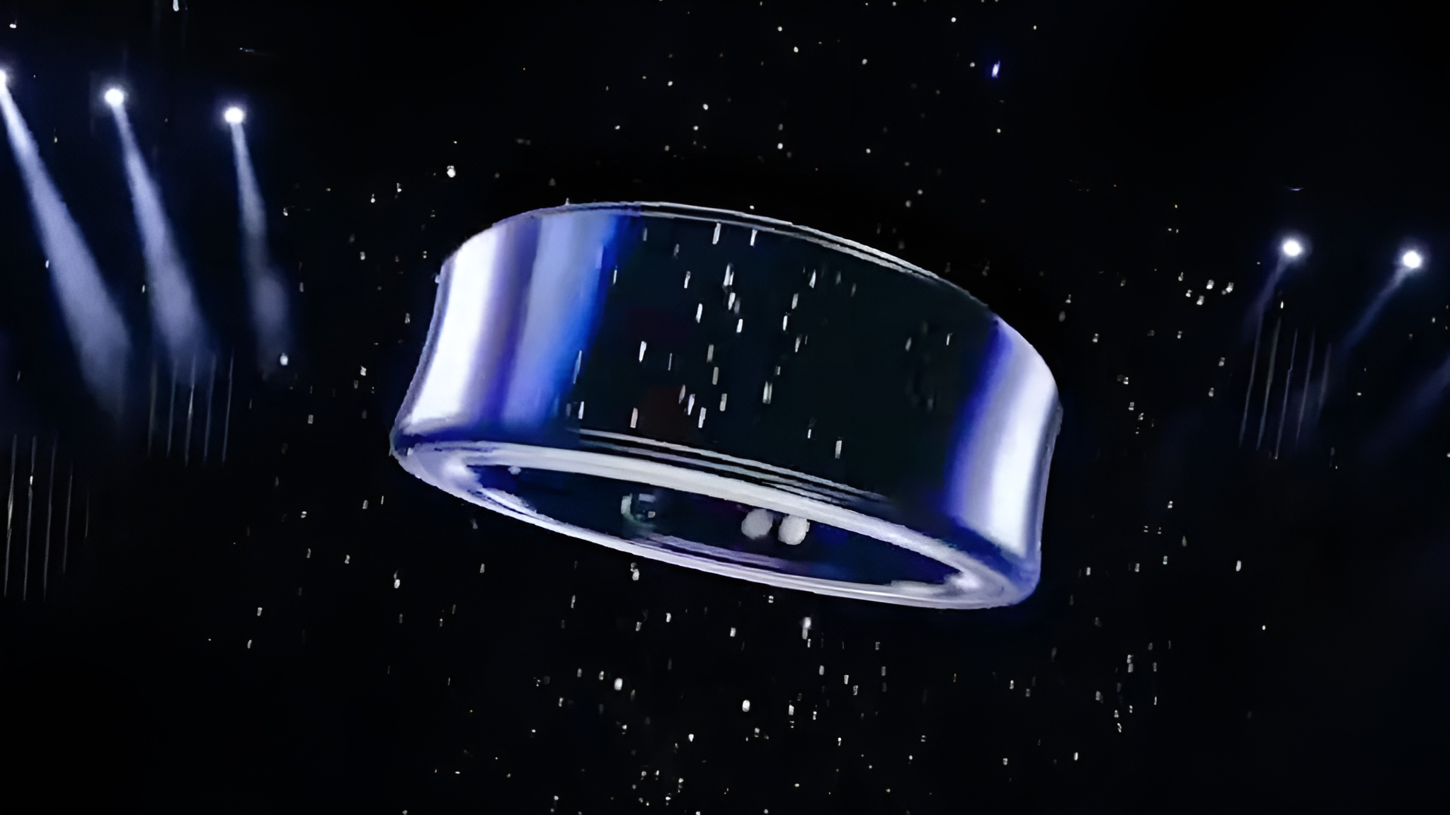 A metallic ring-shaped object is suspended in a dark space with spotlight illumination and a starry background.