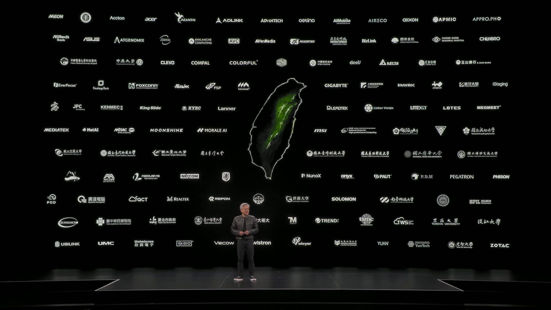 A presenter stands on stage in front of a screen displaying numerous company logos, including Acer, ASUS, GIGABYTE, MSI, and