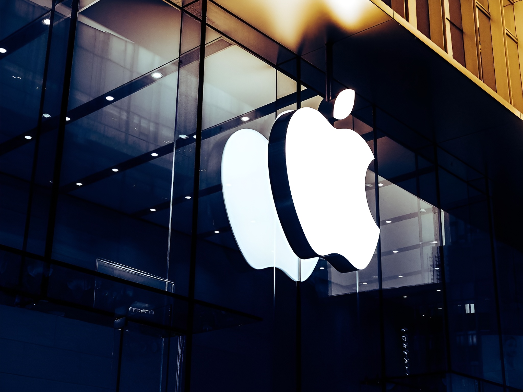 The large illuminated Apple logo on a glass-fronted building reflects city lights.