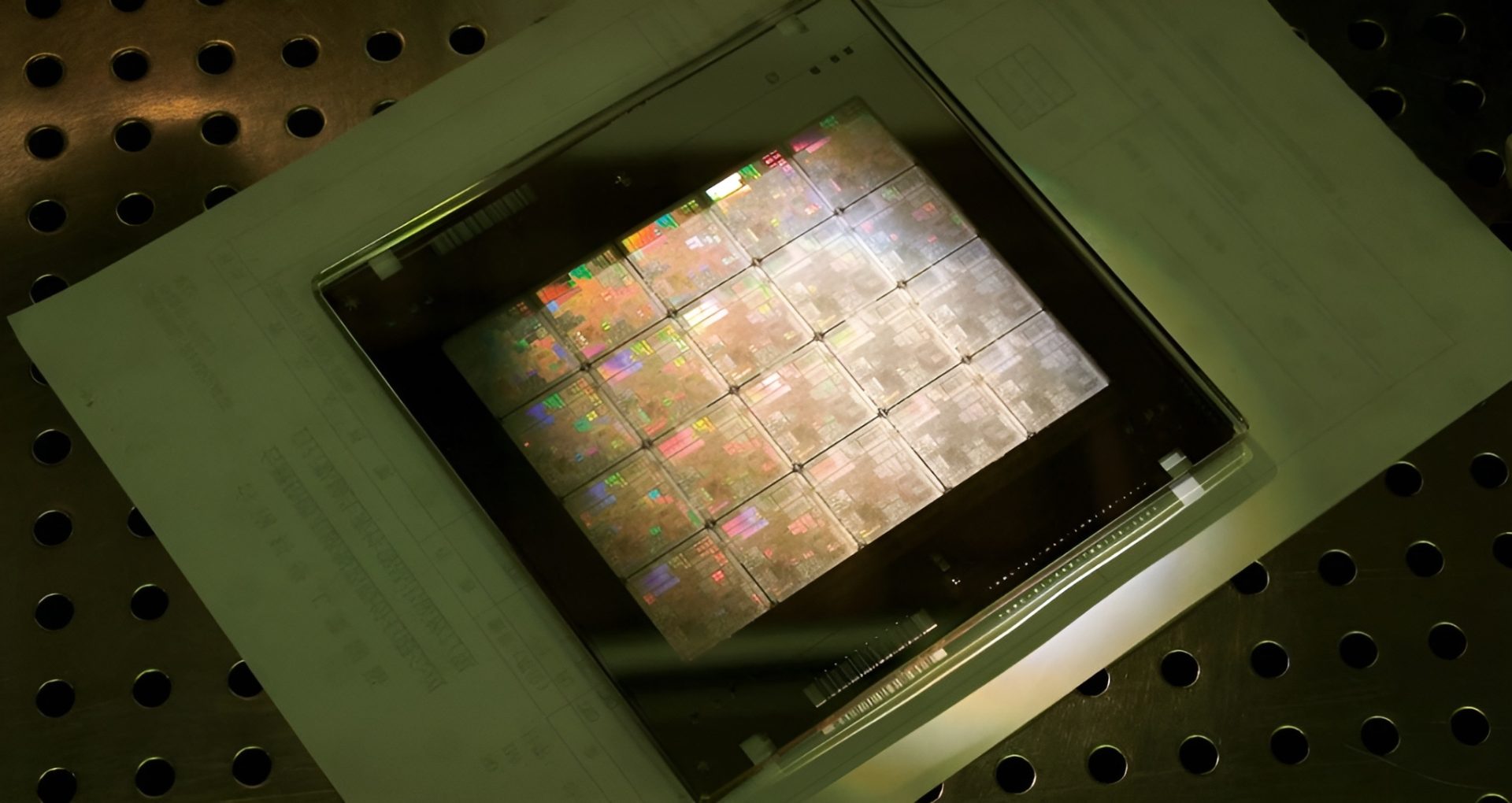A large silicon wafer with multiple microchips is resting on a perforated metal surface.