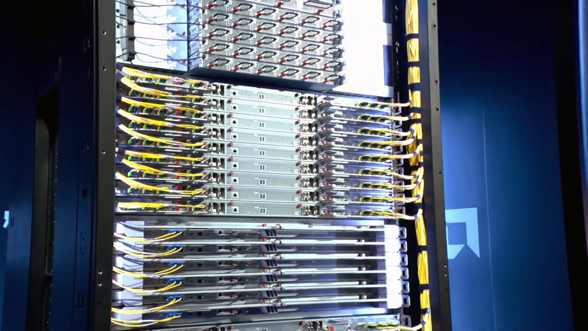 A server rack filled with rows of computing units and yellow cables is displayed, with an AMD logo faintly visible in the