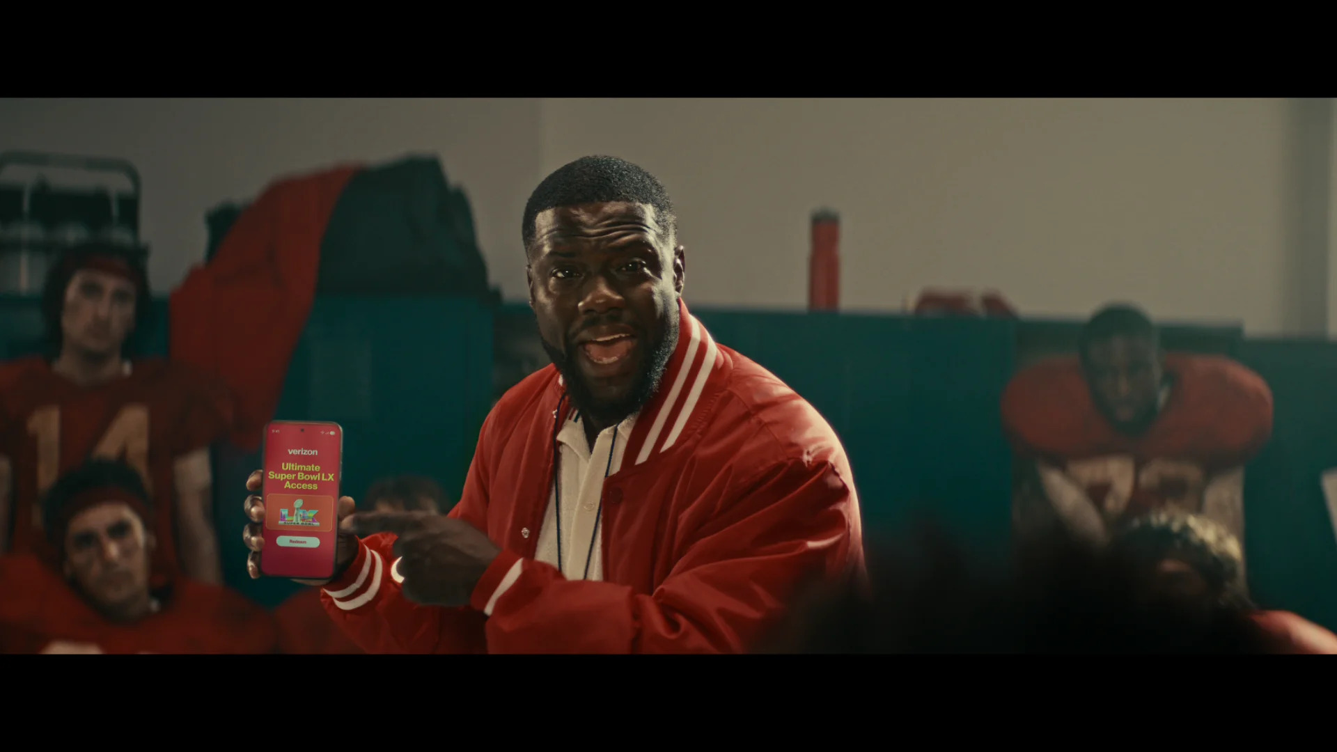 A man in a red jacket holds a smartphone displaying a Verizon app screen with the text 'Ultimate Super Bowl LX Access.'