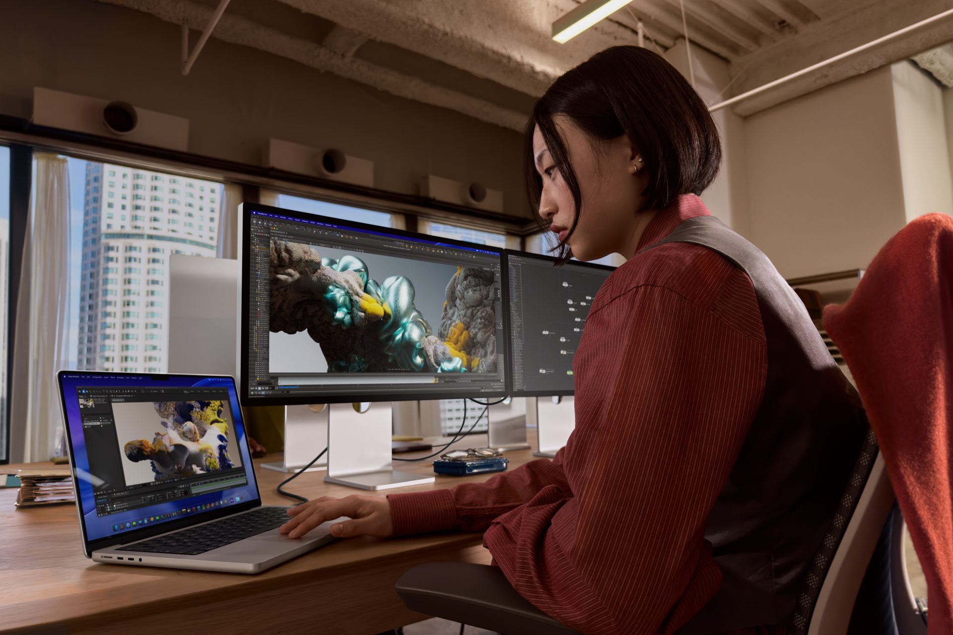 A person working on a MacBook Pro with Maya software displayed on an external monitor.