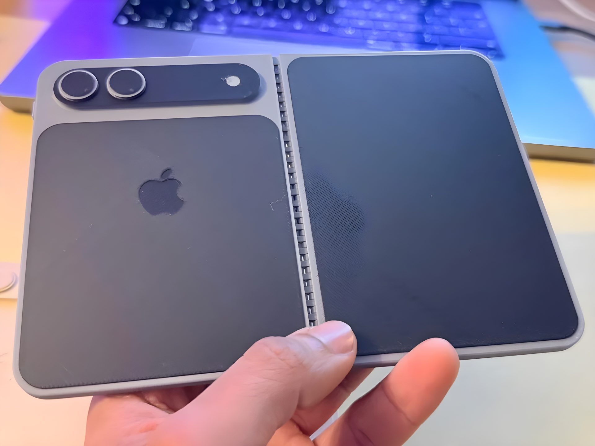 A person is holding a concept model of a foldable Apple device with a dual-camera setup and the Apple logo on the back.