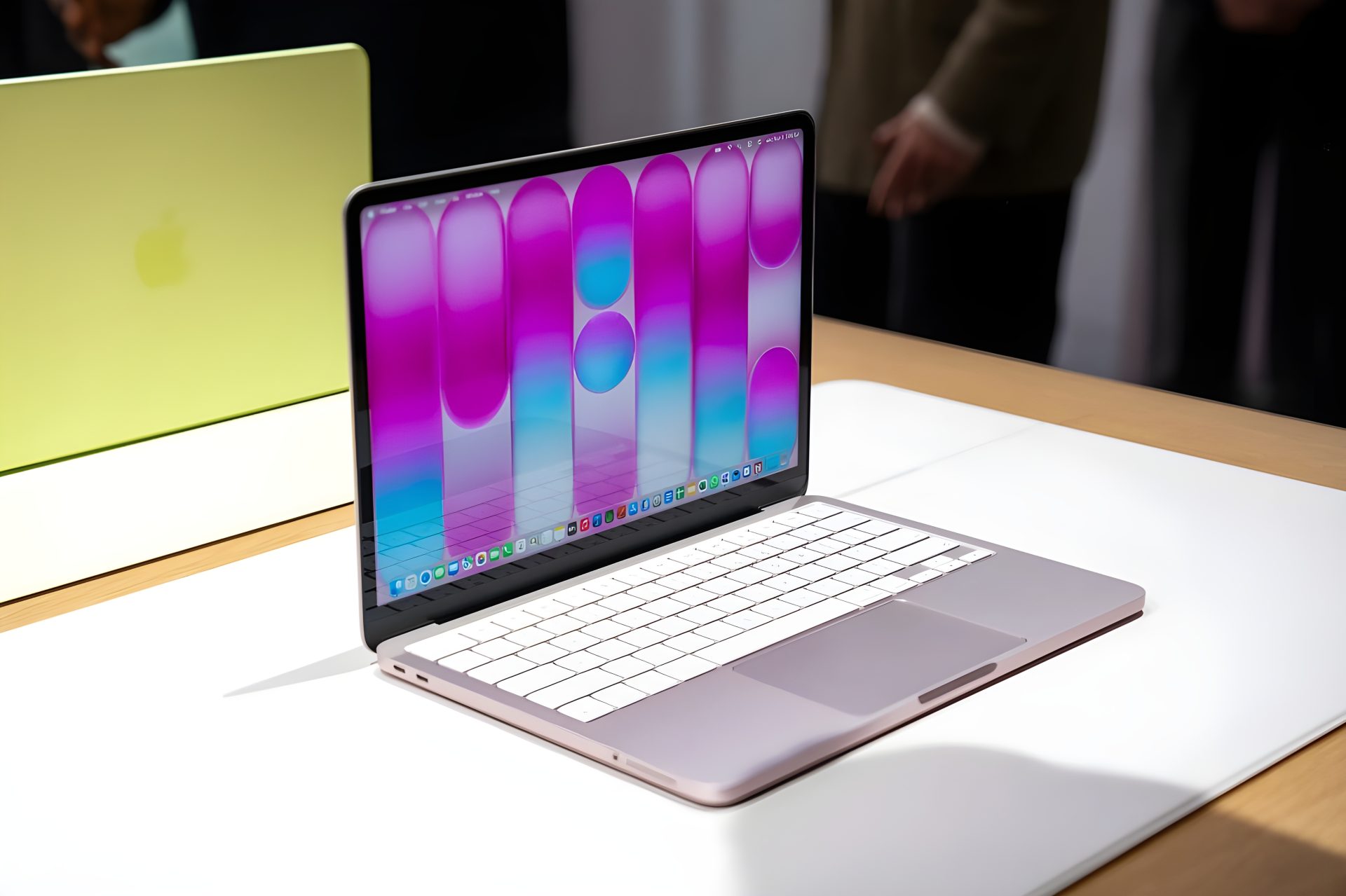 A purple Apple MacBook Air with a colorful abstract wallpaper on its display sits on a white table, with a green Apple
