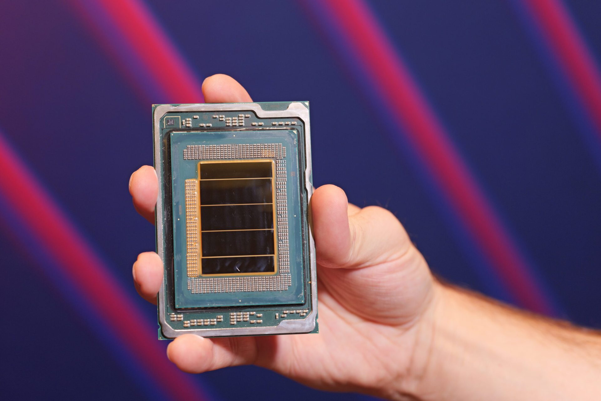 A person holding an Intel processor with a visible die and intricate circuitry, against a blurred background with diagonal