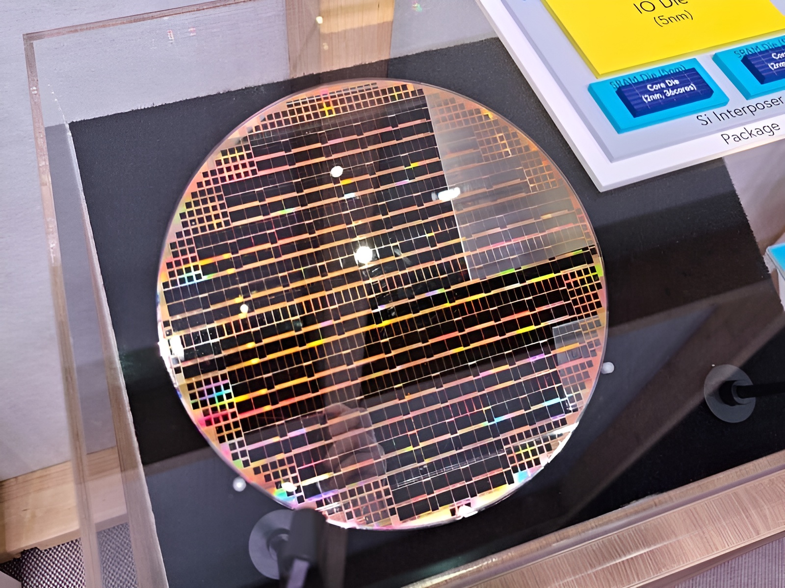 A silicon wafer with intricate circuit patterns is displayed alongside a diagram labeled 'IO Die (5nm)' on an informational sign.