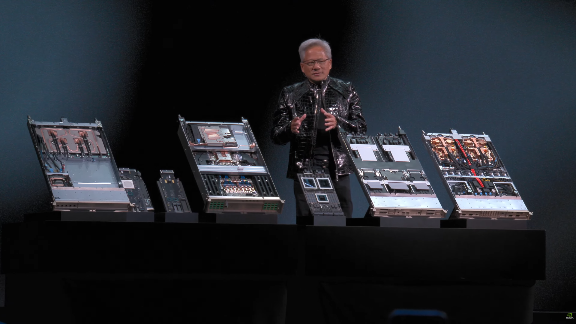 A person is standing on stage showcasing various open server units with visible cooling systems and hardware components.