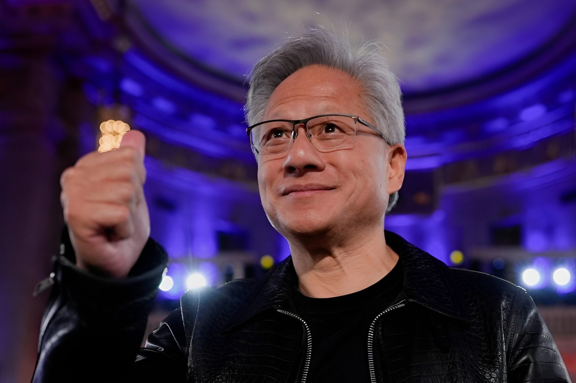 A person in a dark leather jacket is smiling and giving a thumbs-up in front of a softly lit, blue-toned background.