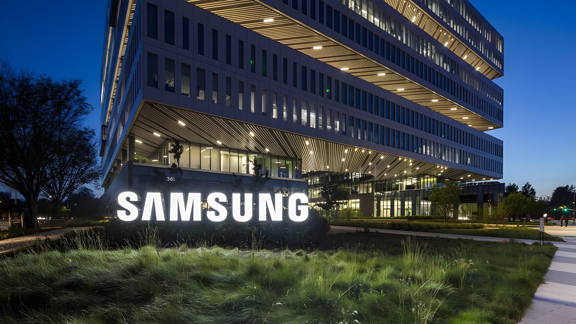 A Samsung office building with a prominent illuminated 'SAMSUNG' sign in front, under a twilight sky.