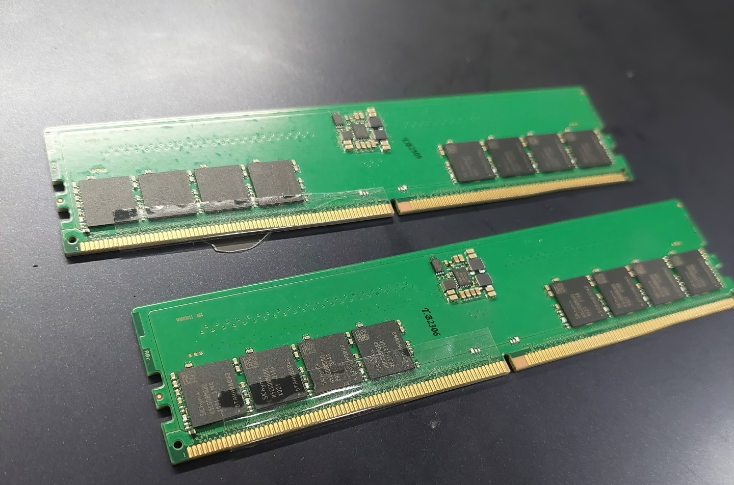 Two unbranded green DDR RAM modules with multiple memory chips and gold contact pins are placed on a dark surface.