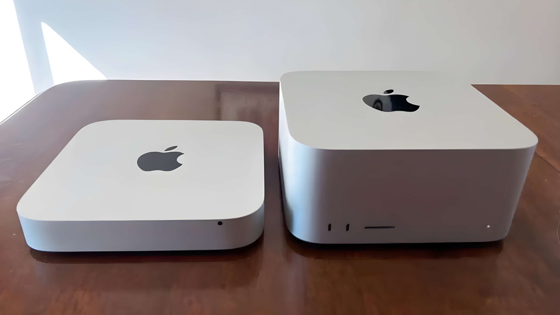 A comparison of the Apple Mac Mini and Mac Studio on a wooden surface.