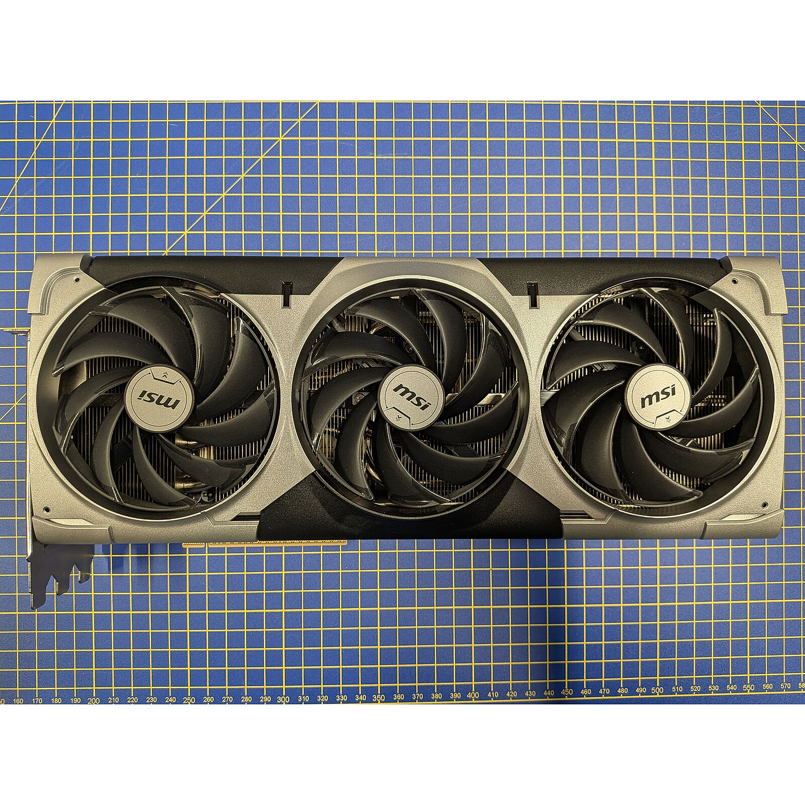 An MSI graphics card with three large cooling fans is displayed on a blue grid-patterned mat.