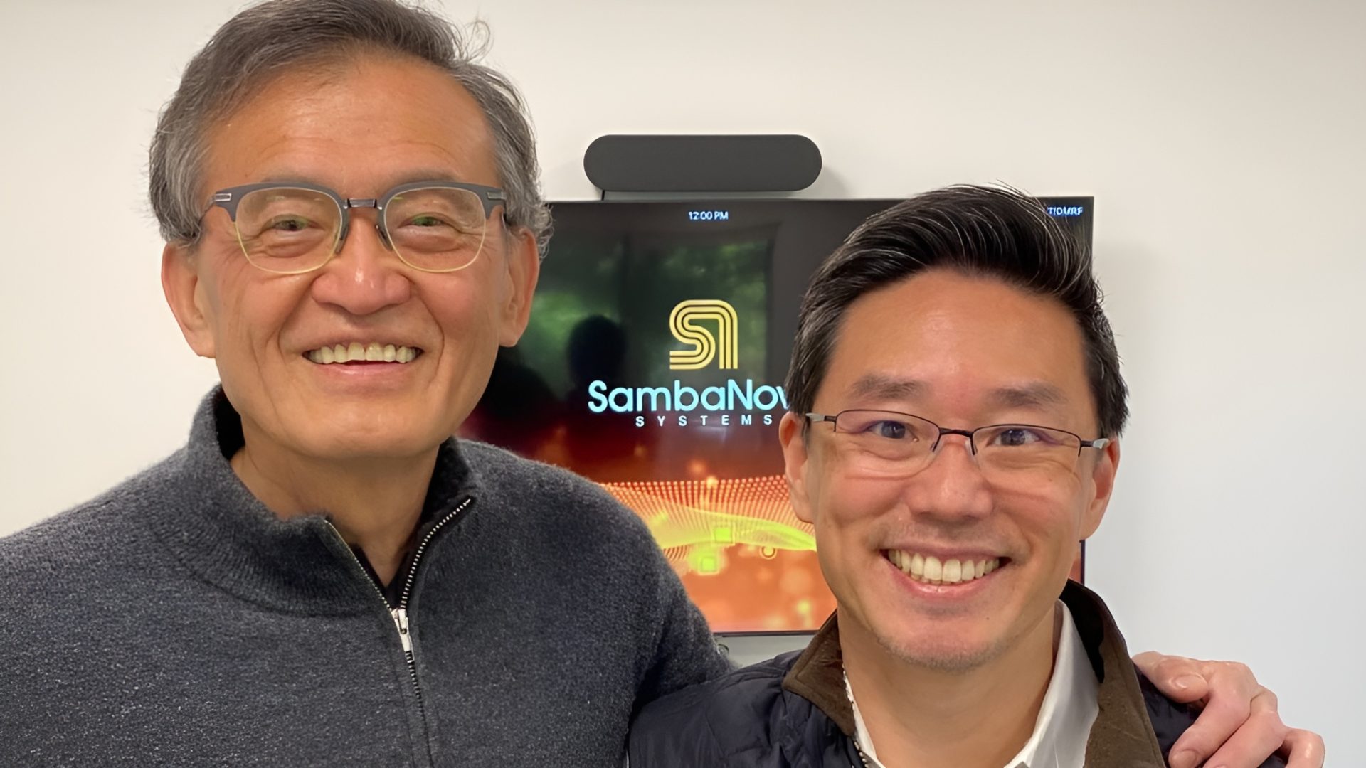Two smiling individuals stand in front of a screen displaying the 'SambaNova Systems' logo.