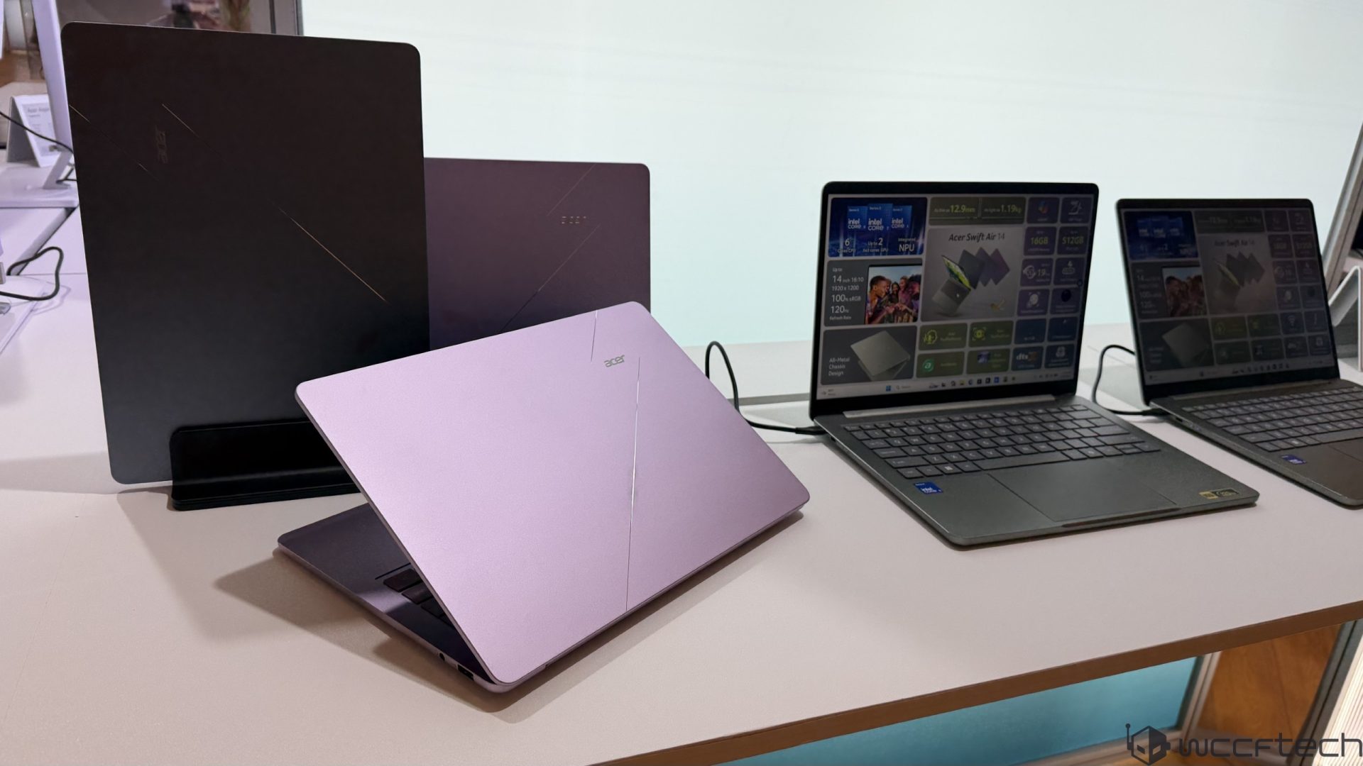 Three Acer laptops are displayed on a table, including an open Acer Swift Air 14+ showing detailed specifications on its screen.