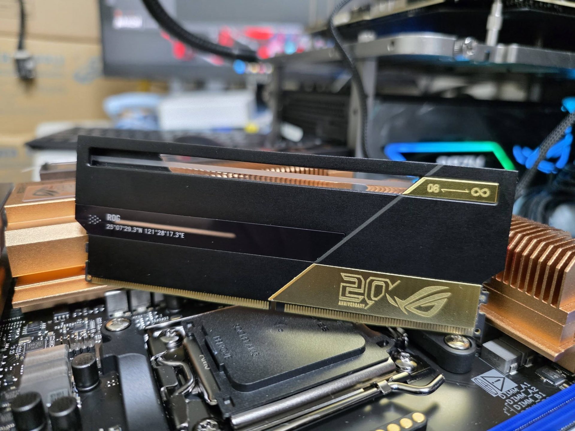 An ASUS ROG 20th Anniversary RAM module is installed on a motherboard, with visible coordinates '25°07'29.3N 121°28'17.3E' and a gold 20th-anniversary emblem.