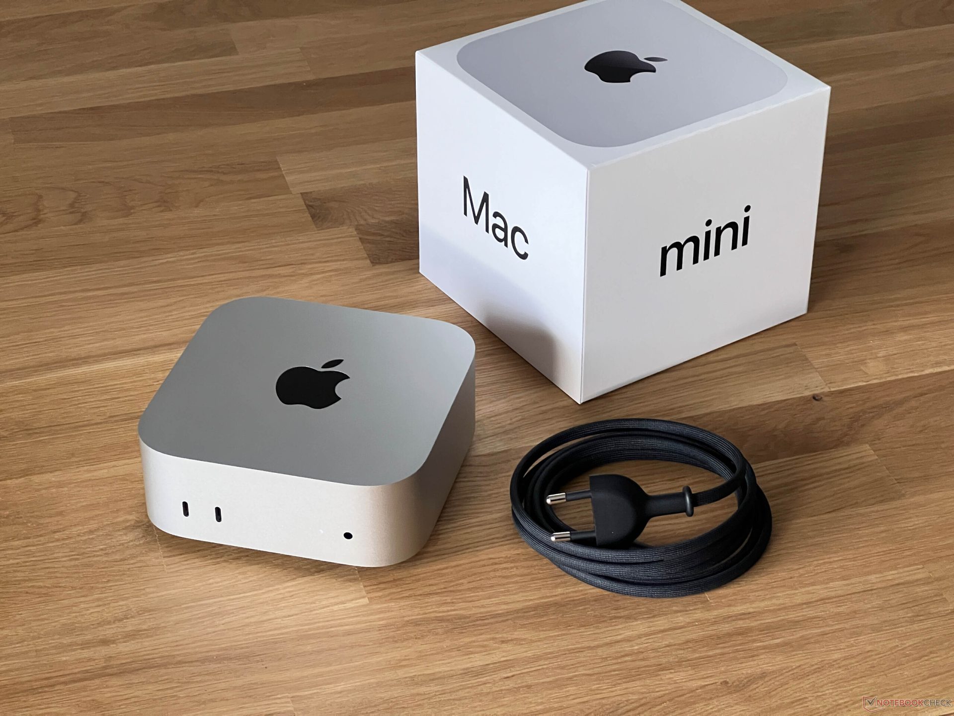 Apple Mac mini with its box and power cable on a wooden surface.