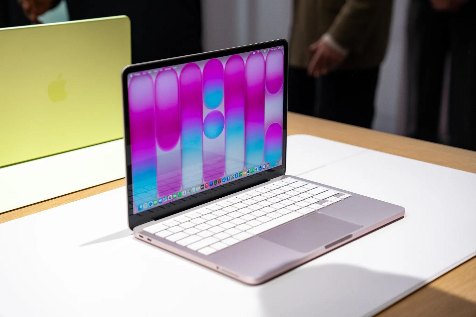 An Apple MacBook is open on a table, displaying a colorful abstract background, with another closed MacBook in yellow