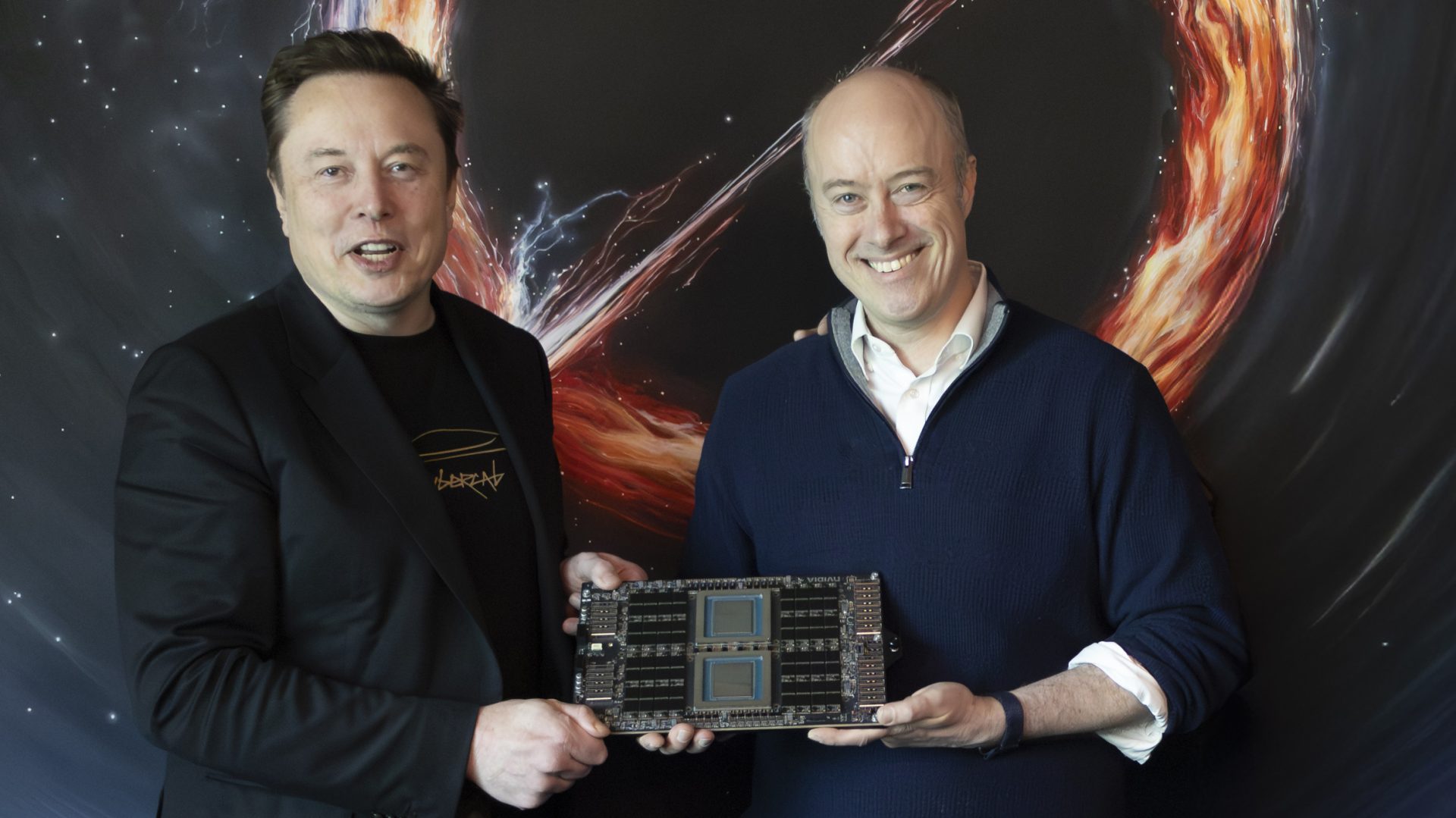 Two smiling men holding a large computer chip with dark circuitry, standing against a colorful cosmic background.
