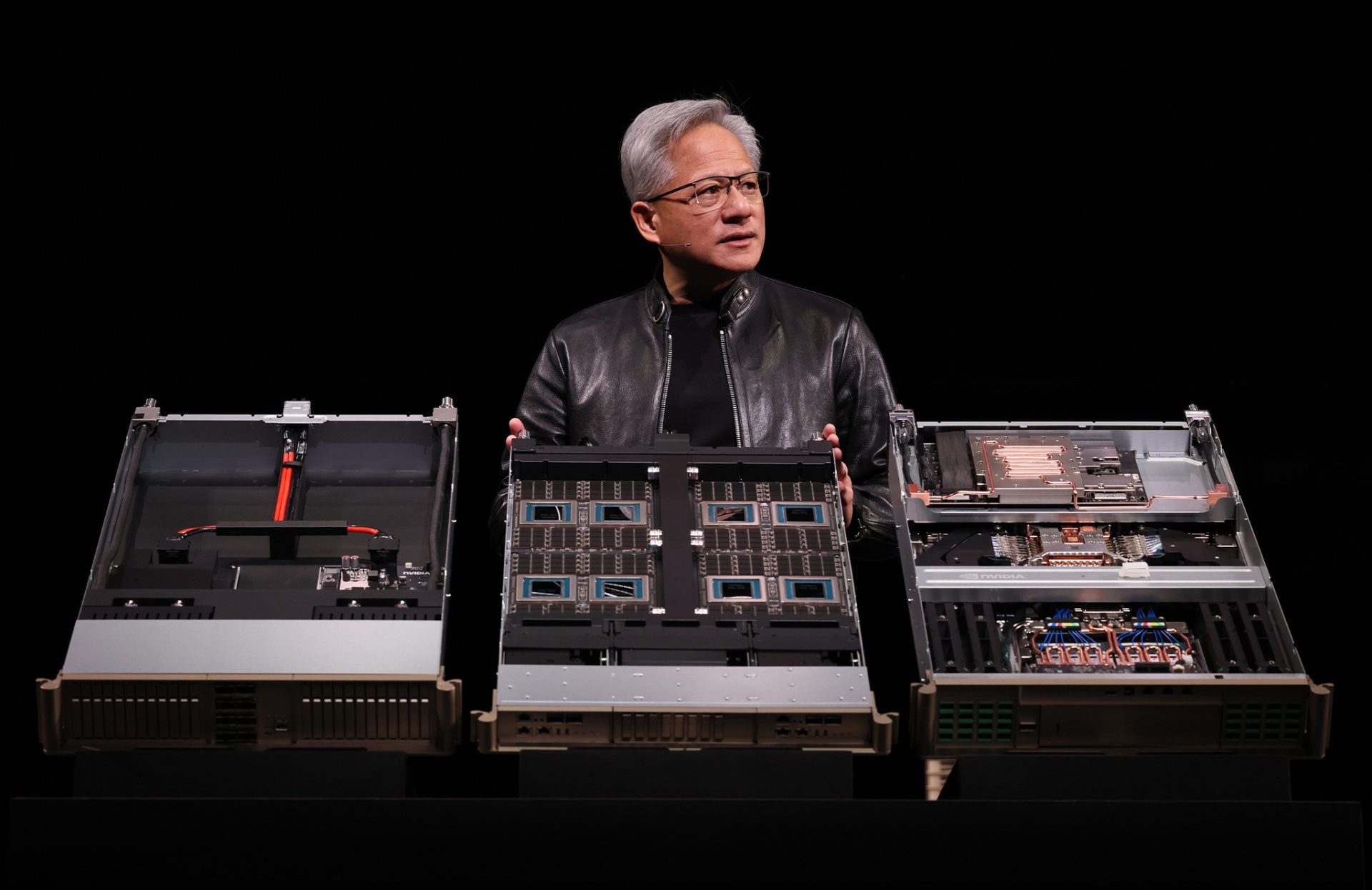 A person is holding NVIDIA server hardware at a presentation, showcasing multiple circuit boards with visible chipsets.