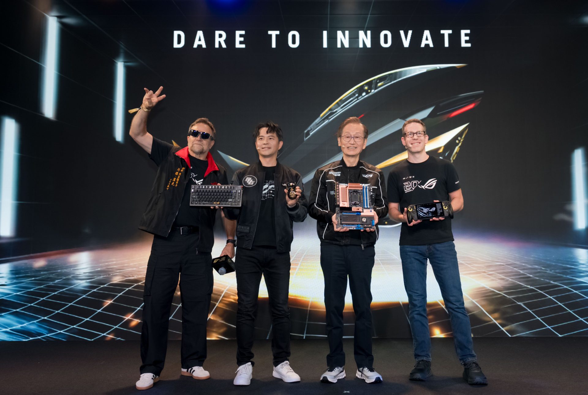 Four individuals stand on stage under 'DARE TO INNOVATE', holding various ASUS ROG products, including a keyboard, a headset, a motherboard, and a handheld gaming device.