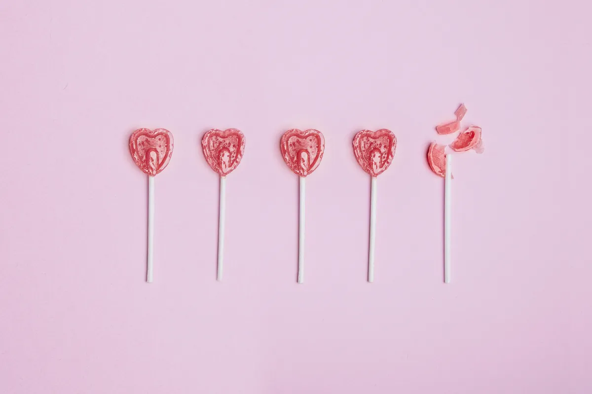 Five lollipop hearts on a pink floor, but the last one is smashed to pieces.