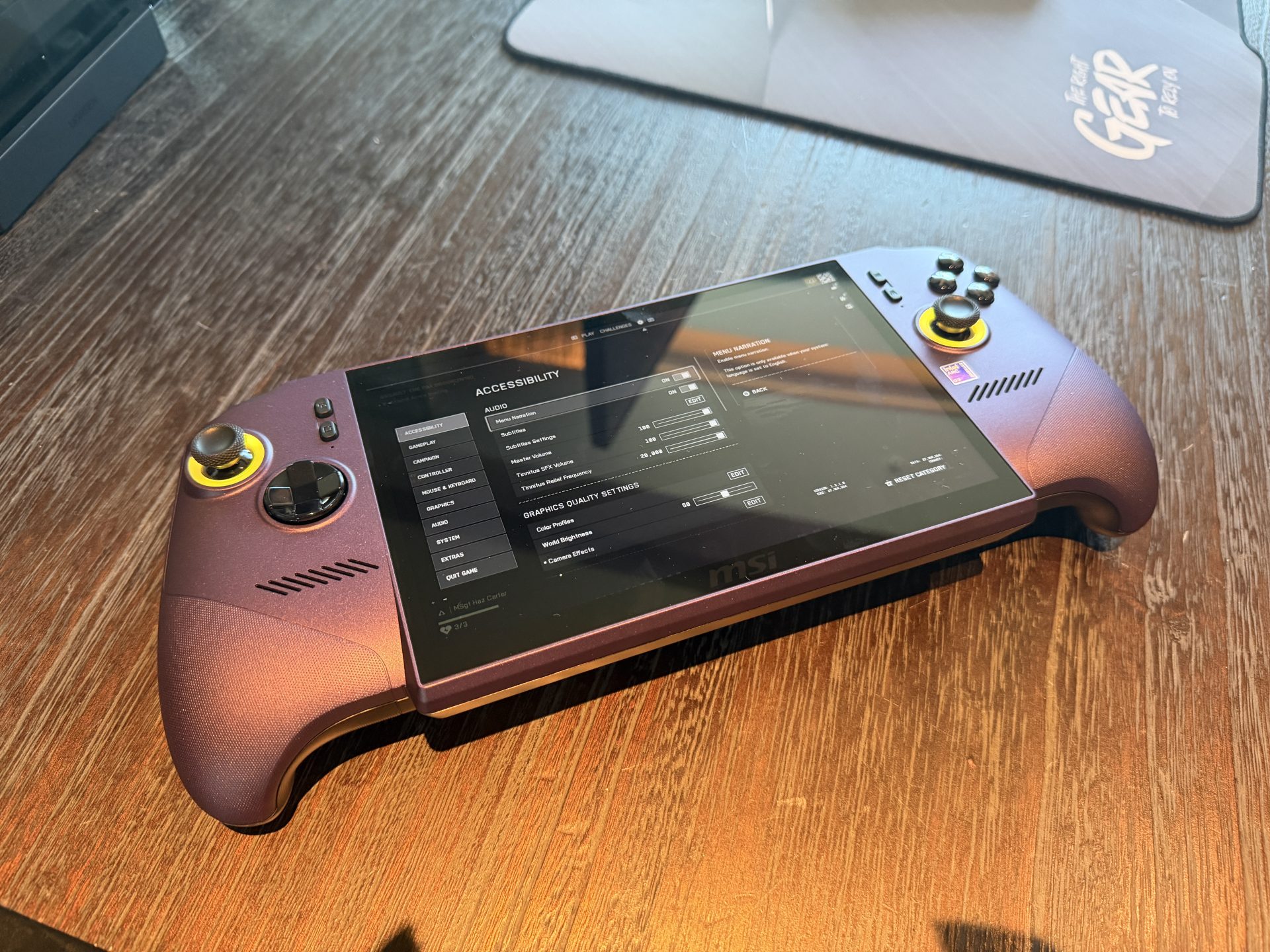 An MSI handheld gaming device is displayed on a wooden table showing an