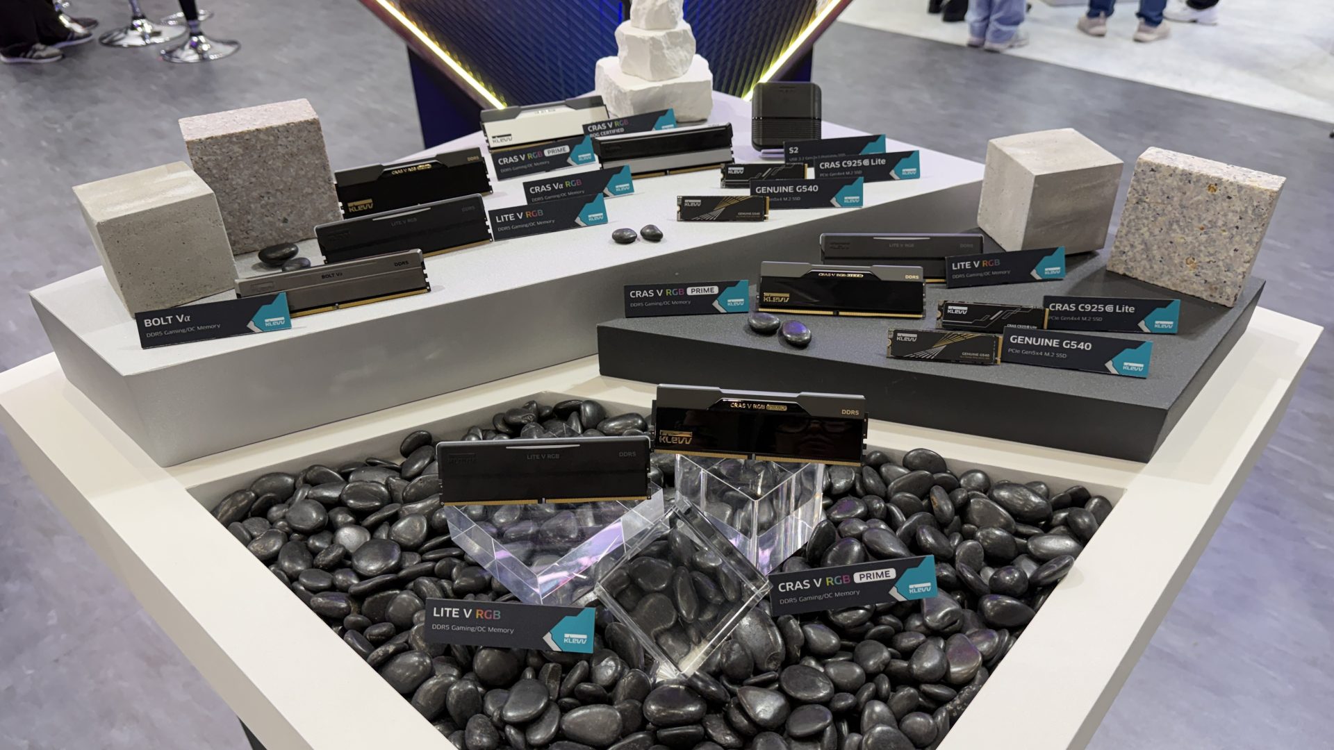 KLEVV DDR5 RAM modules and SSDs, including the 'BOLT Vα', 'LITE V RGB', 'CRAS V RGB', and 'GENUINE G540', are displayed on a table surrounded by decorative stones.