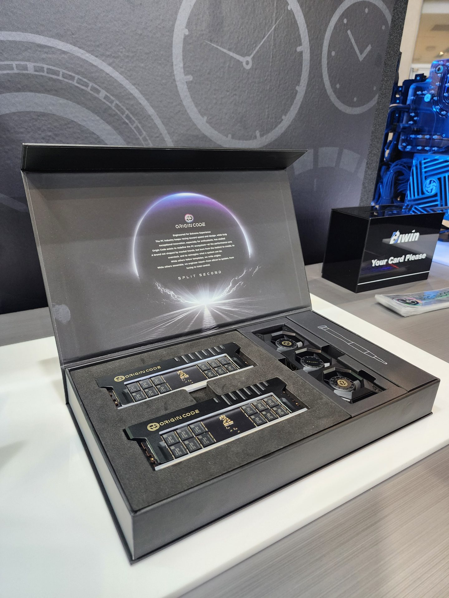 A box containing two Origin Code branded components and cooling fans is displayed on a table.