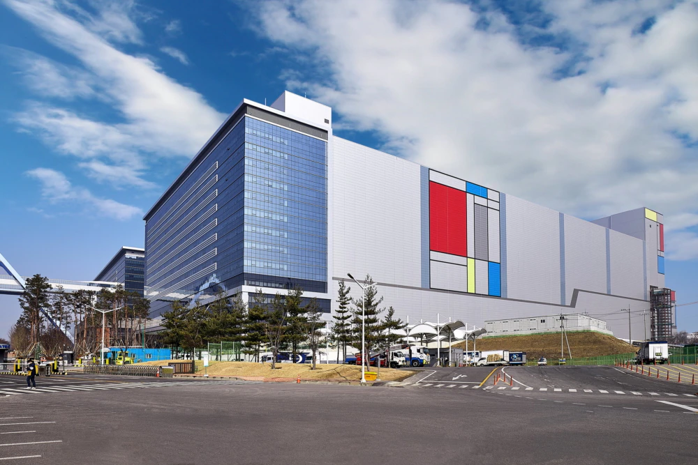 A large, modern Samsung semiconductor manufacturing facility with colorful geometric patterns on the facade and a clear sky in the background.