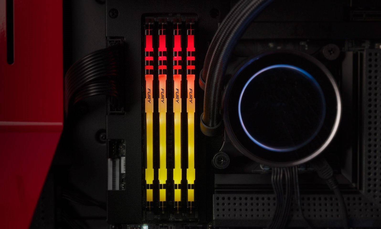 Four Kingston Fury RGB RAM modules with red and orange lighting are installed in a PC motherboard next to a liquid cooling system.