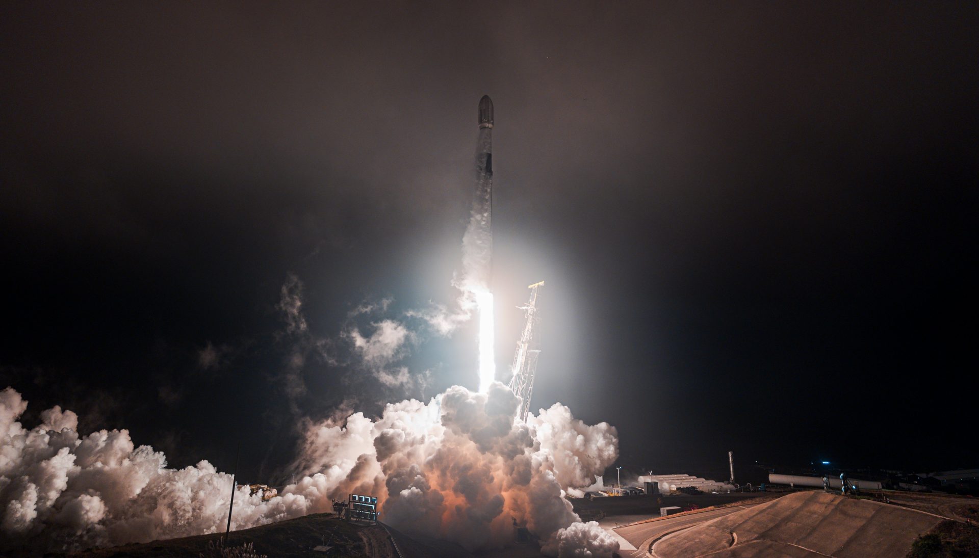 A rocket launches into the night sky surrounded by smoke.